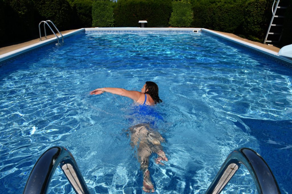 A female swimming laps for exercise in an outdoor pool.